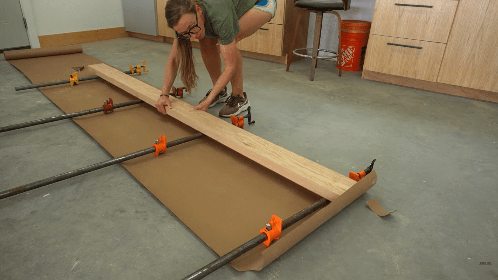 a woman aligning wooden boards with clamps on a workshop floor while working on a woodworking project