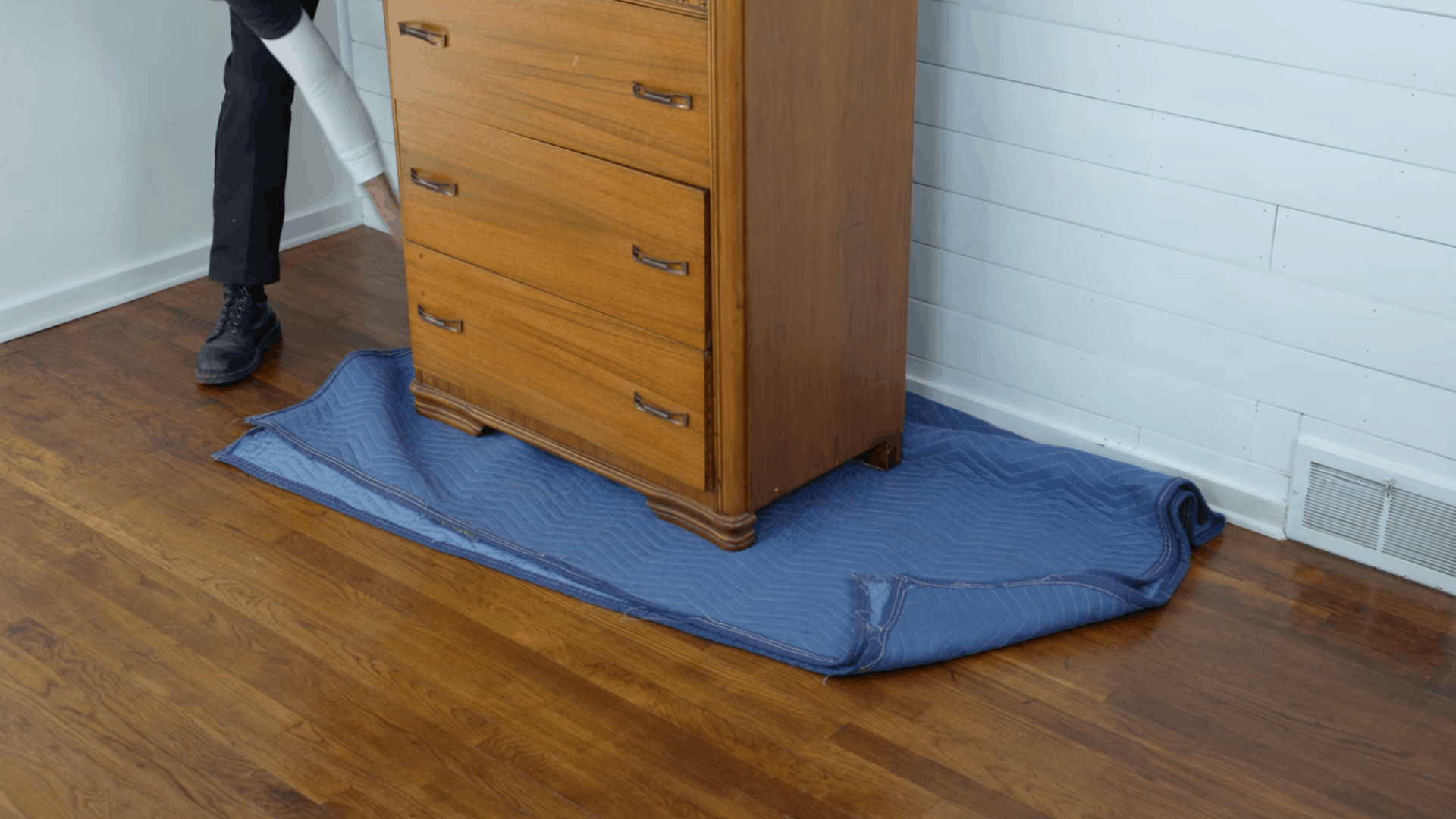 adjusting a moving pad around a wooden dresser to protect the floor during furniture moving