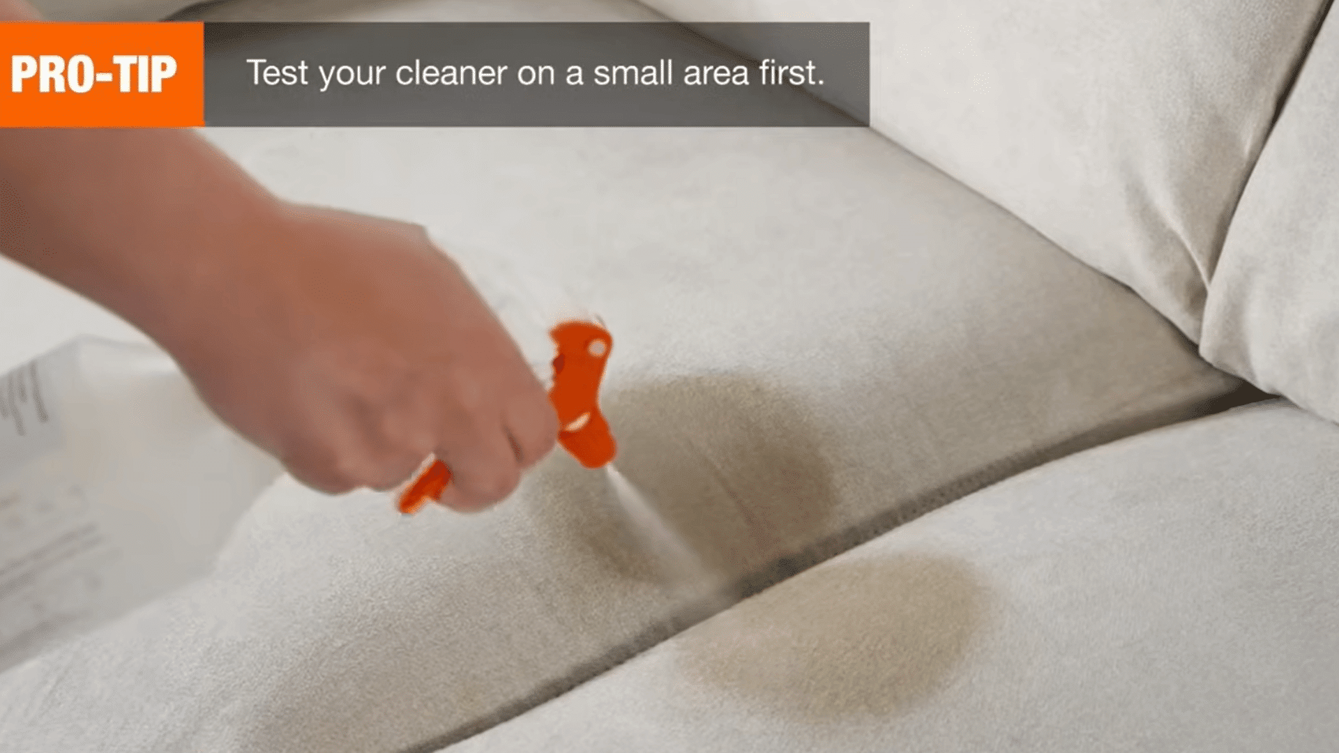 cleaning cloth spray bottle and brush placed on a beige sectional sofa in a bright living room