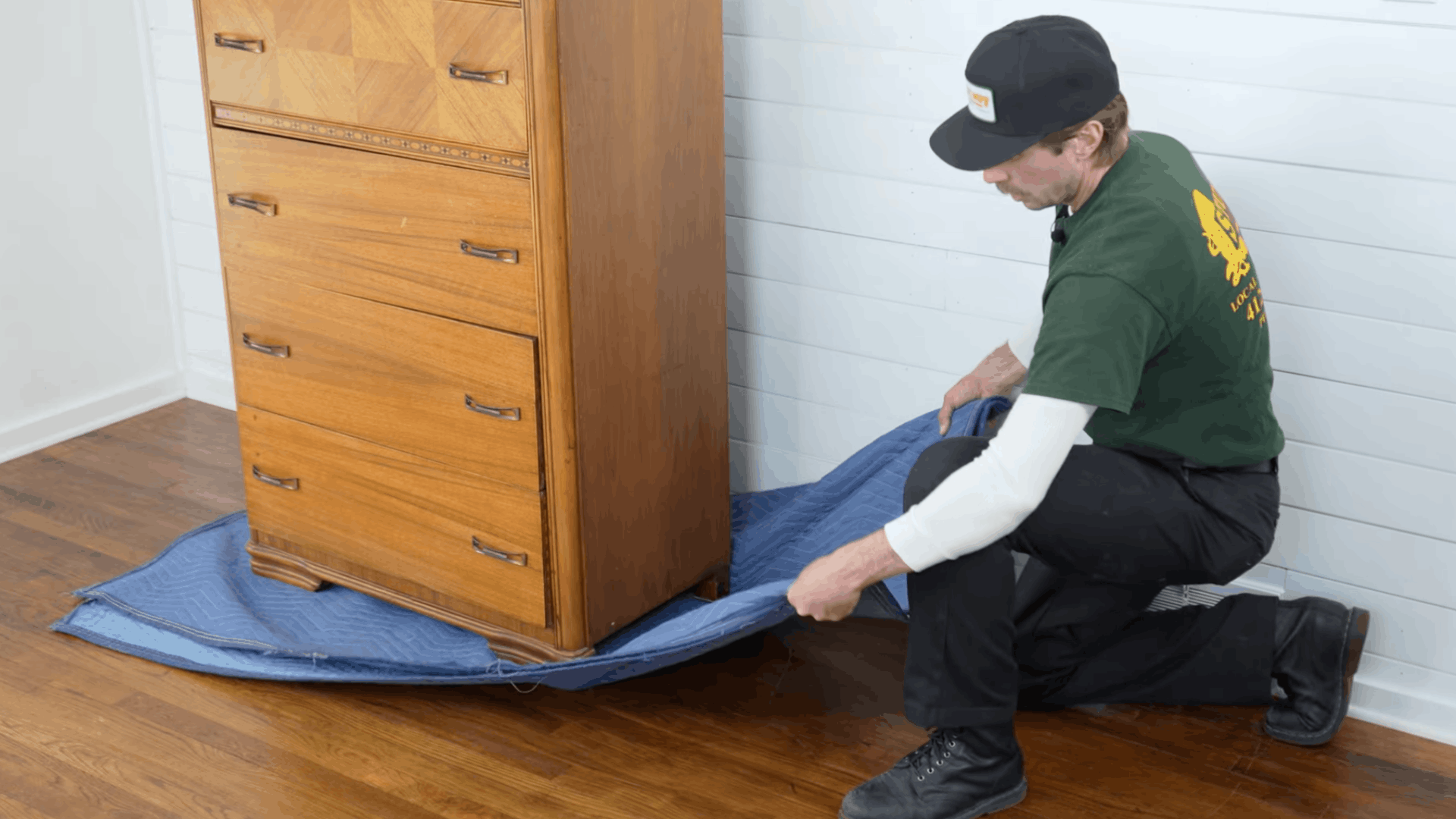 person kneeling beside a wooden dresser pulling a moving pad slowly to keep furniture movement controlled
