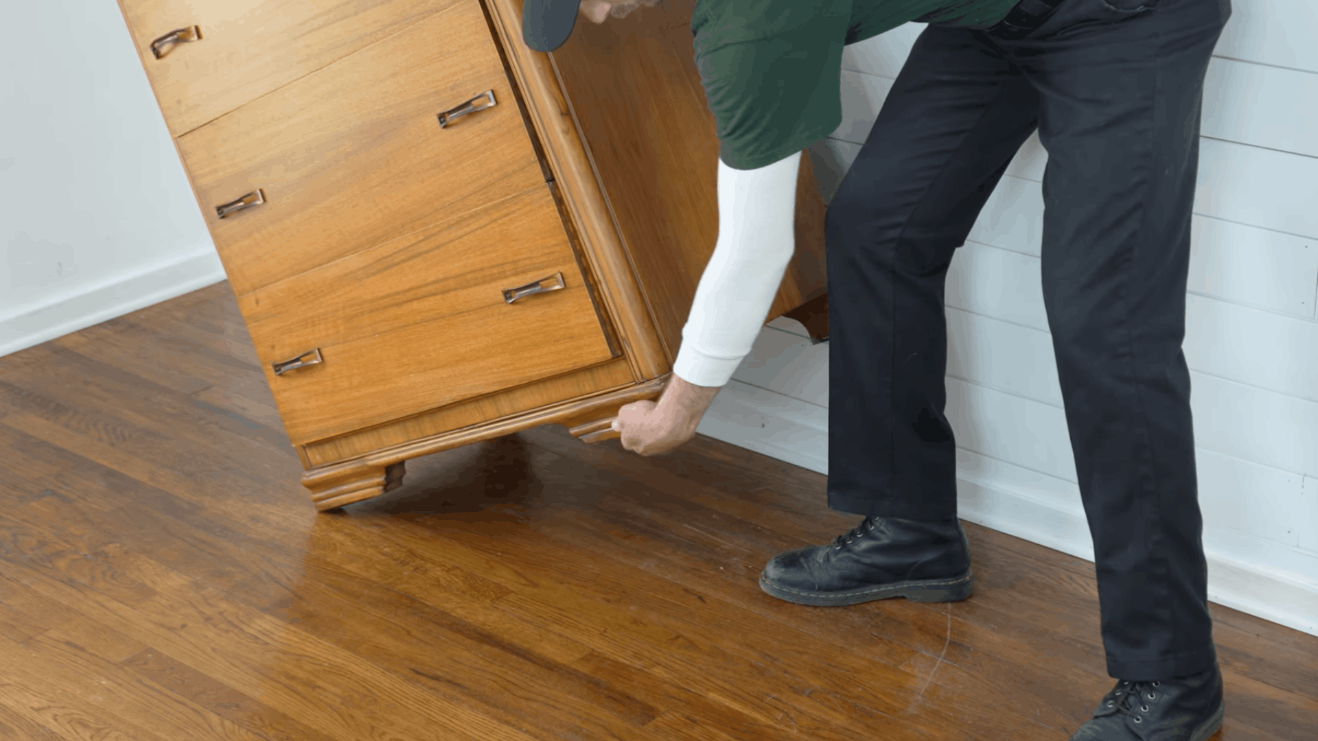 person lifting a wooden dresser to inspect the bottom before moving furniture safely