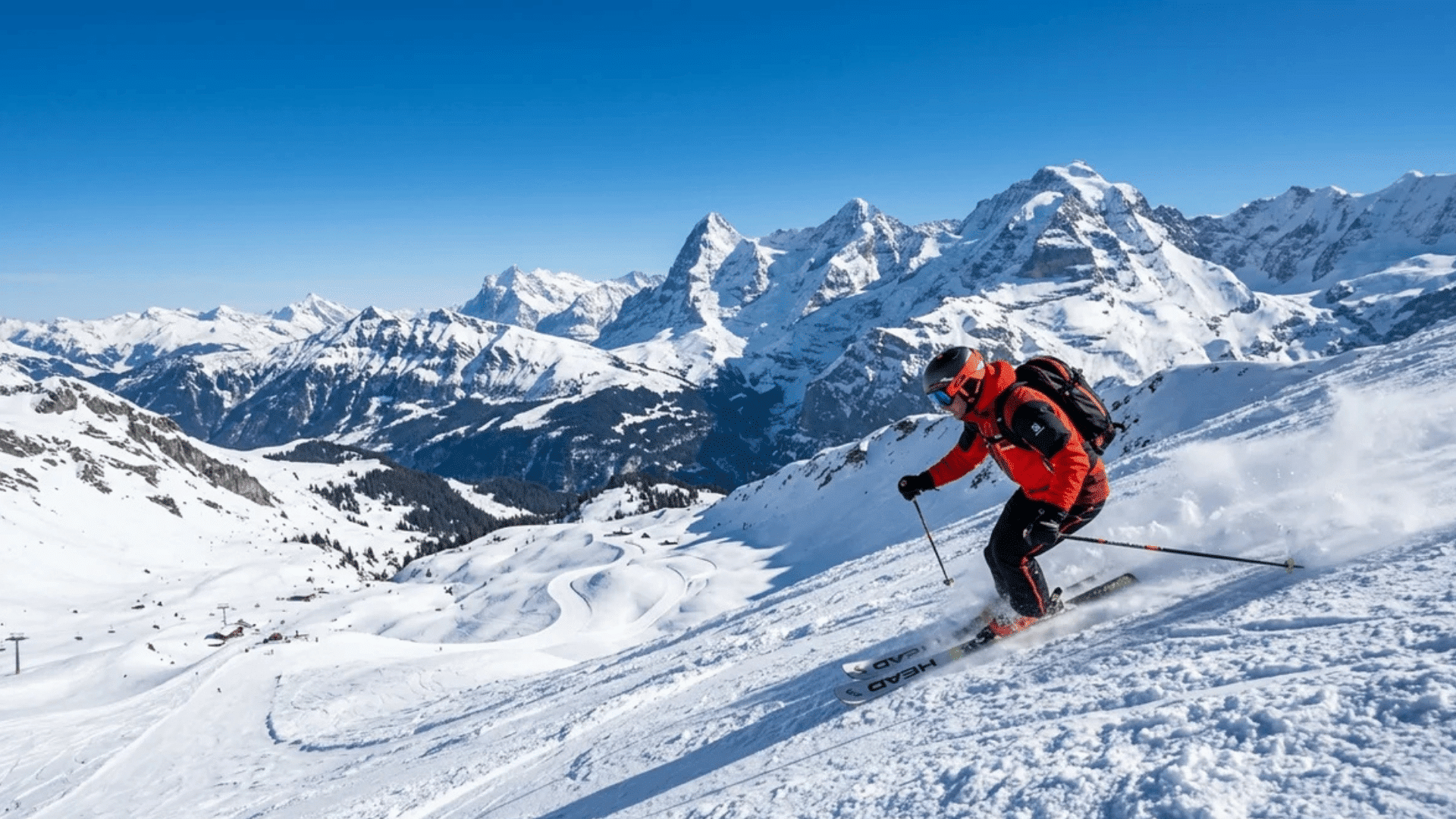 skier in red jacket skiing down snowy mountain slope with high peaks and clear blue sky in winter landscape