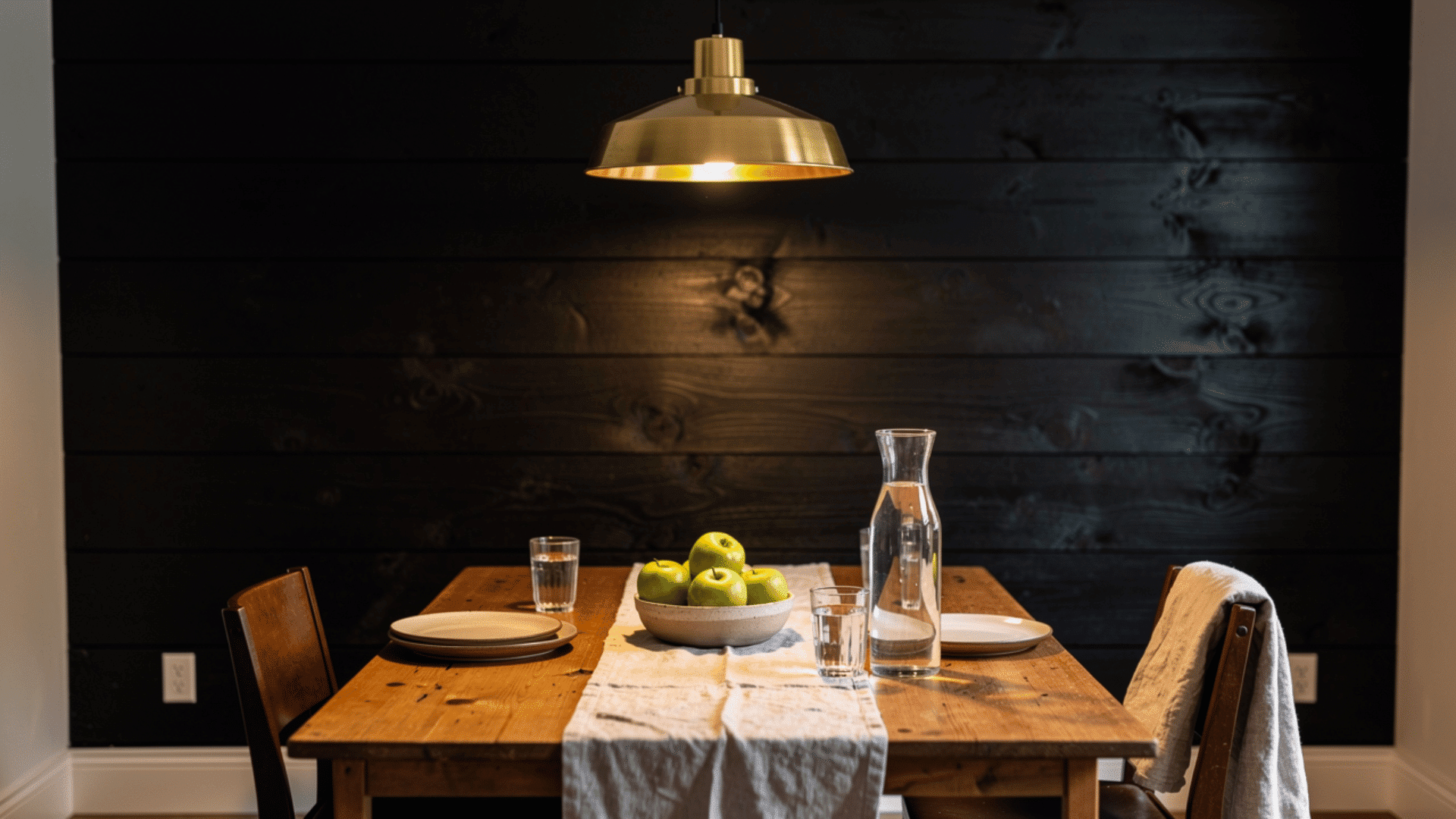 black stained wood plank wall in a dining room with brass pendant light and wooden table