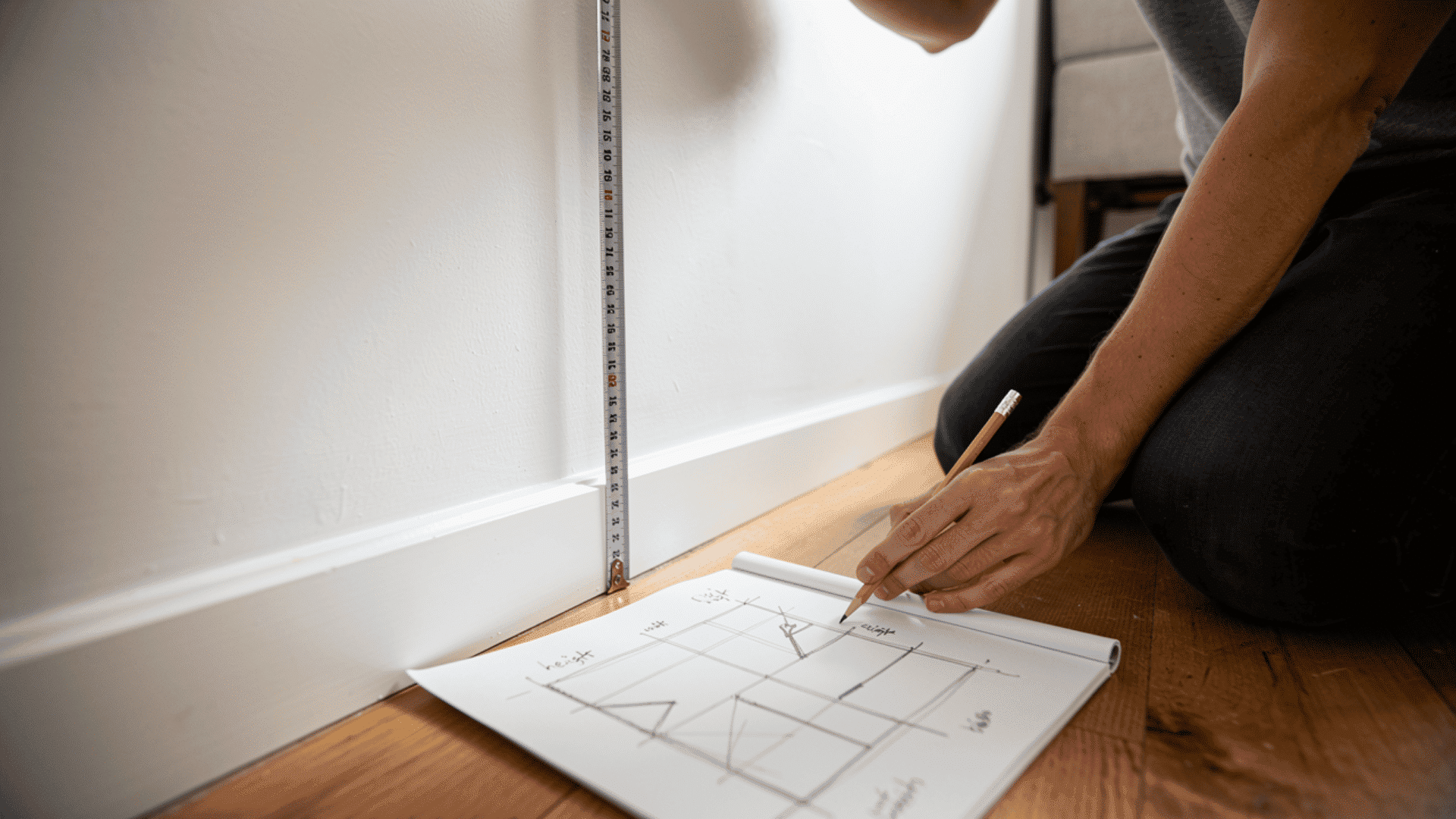 person measuring wall and sketching geometric layout on notepad