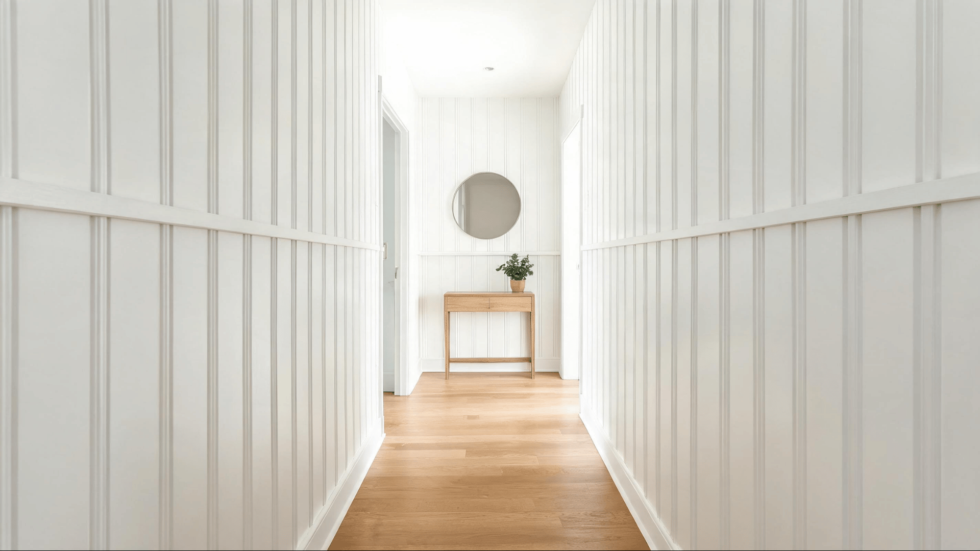 white board and batten accent wall in a bright hallway with a console table and round mirror
