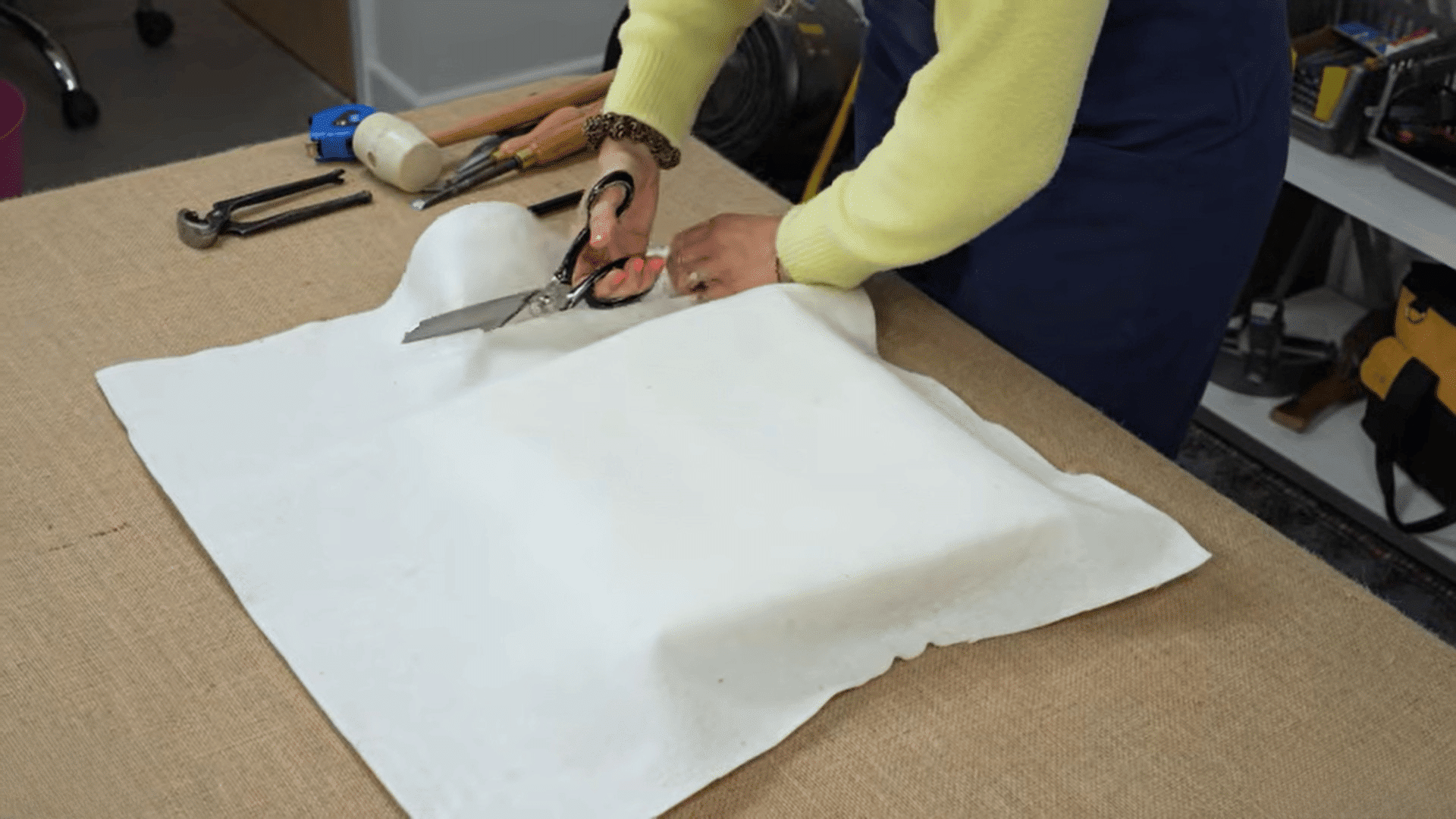 woman cutting fabric padding to reupholster dining chairs on worktable