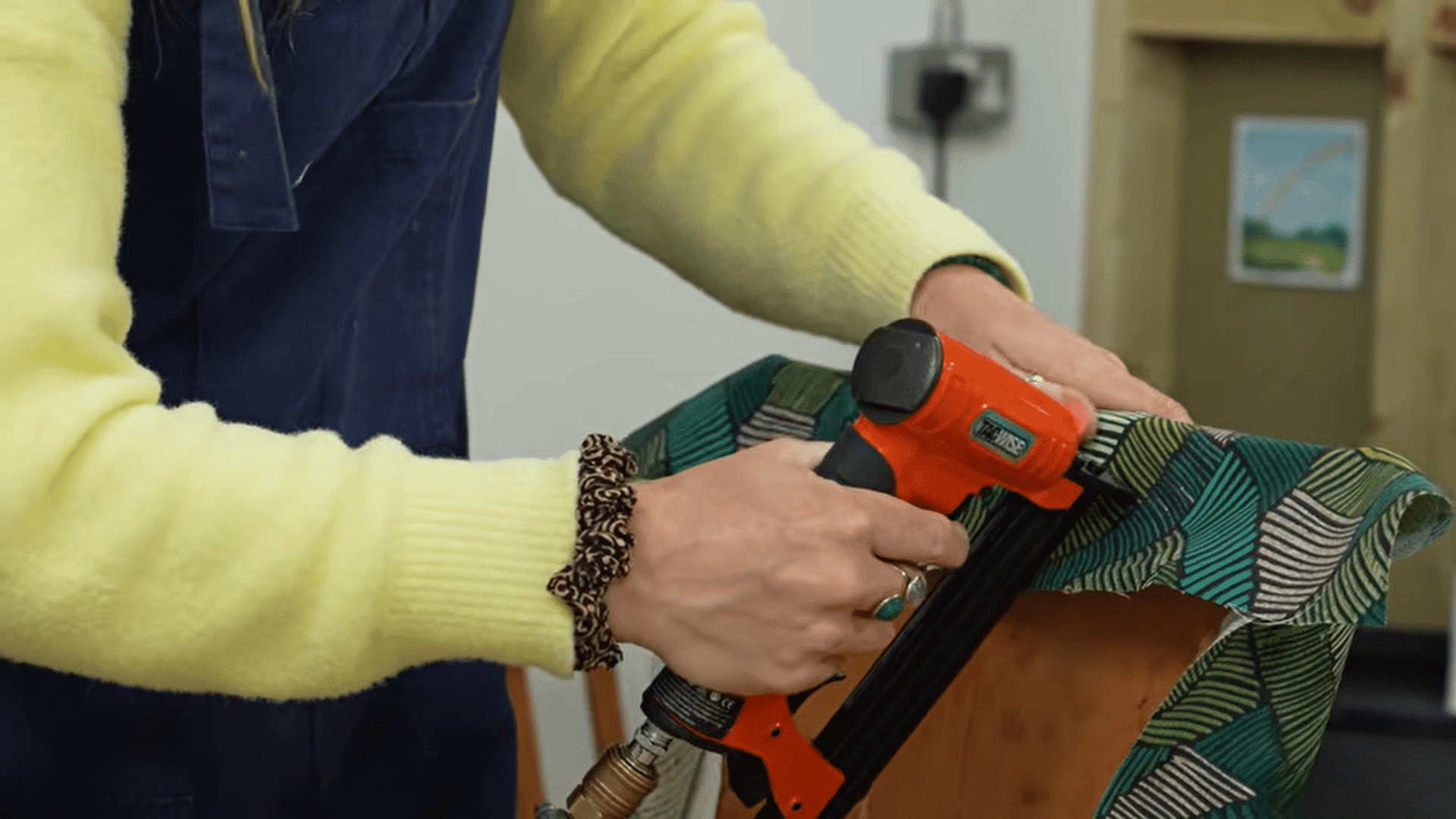 woman using staple gun to reupholster dining chairs with patterned fabric