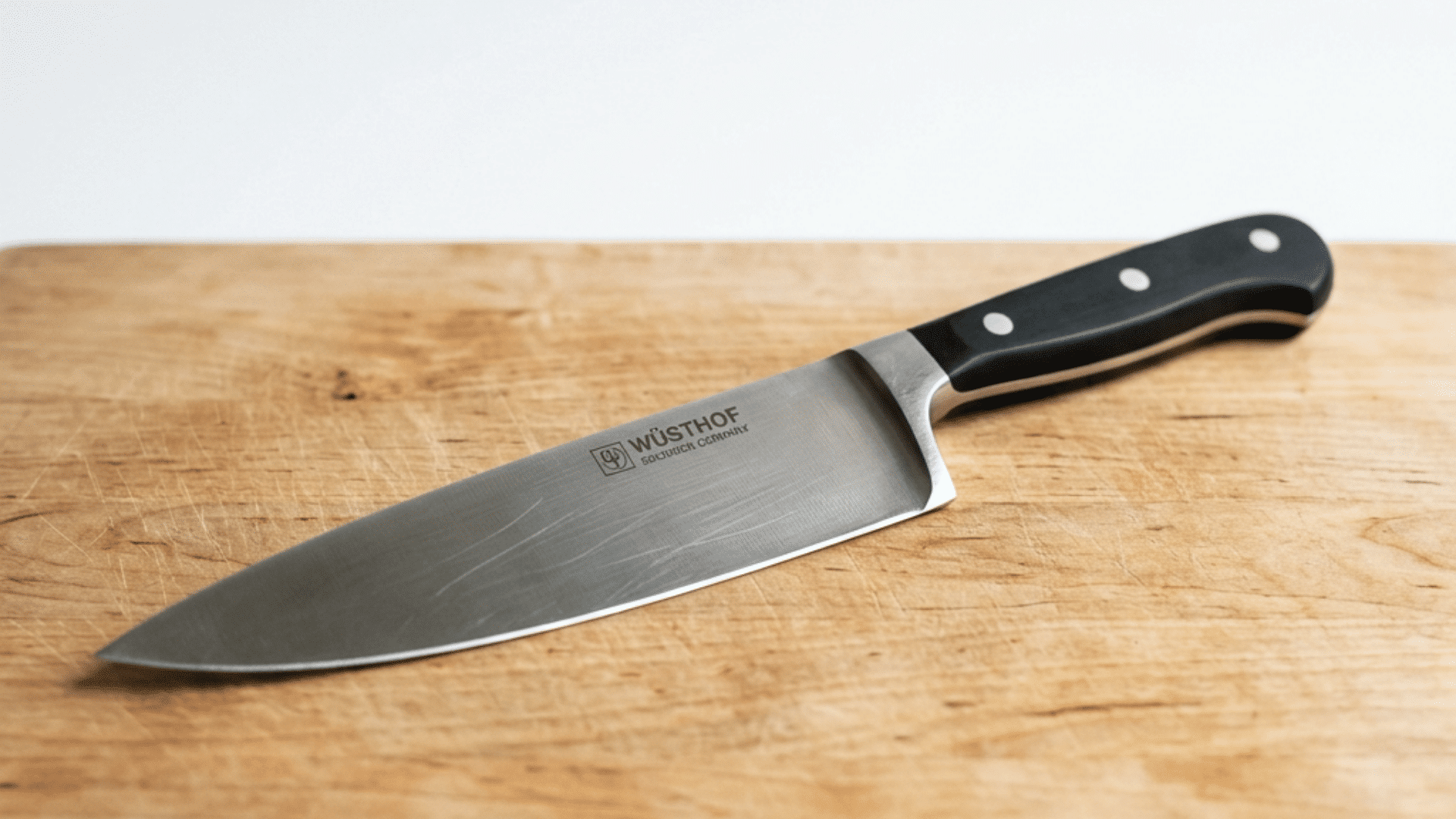 a single chefs knife resting on a light wood cutting board with a clean white background and soft natural light