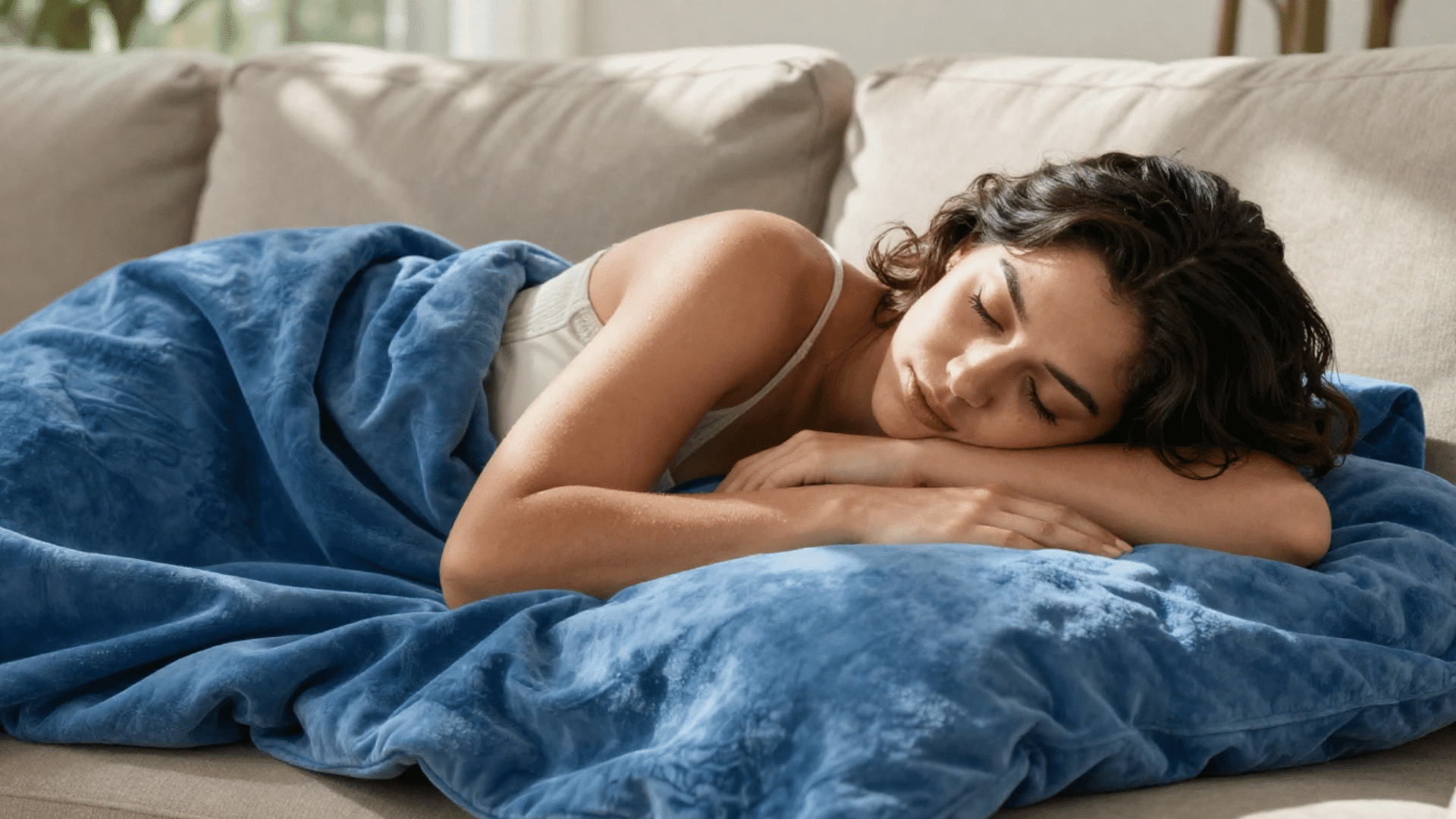 a woman is sleeping peacefully on a beige couch covered by a soft blue blanket