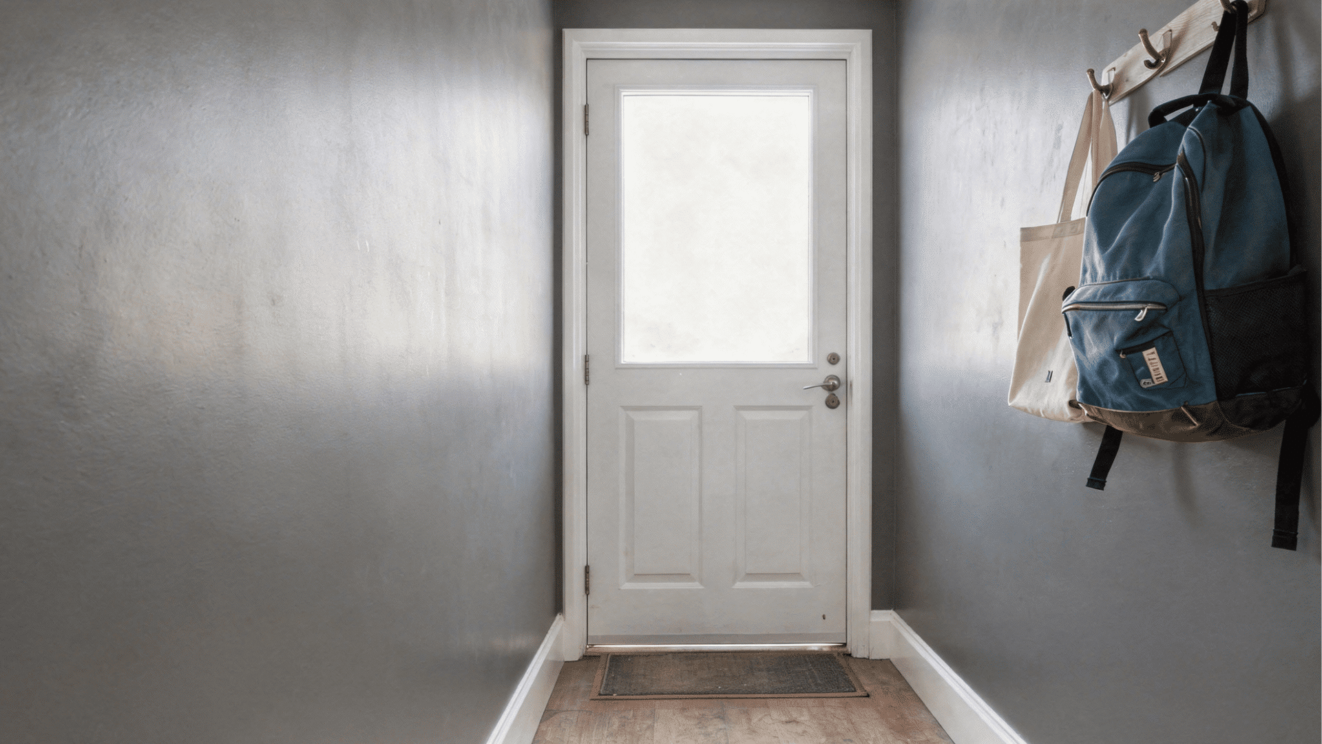 blue backpack and a canvas tote bag hang on hooks next to a white door with a frosted glass pane