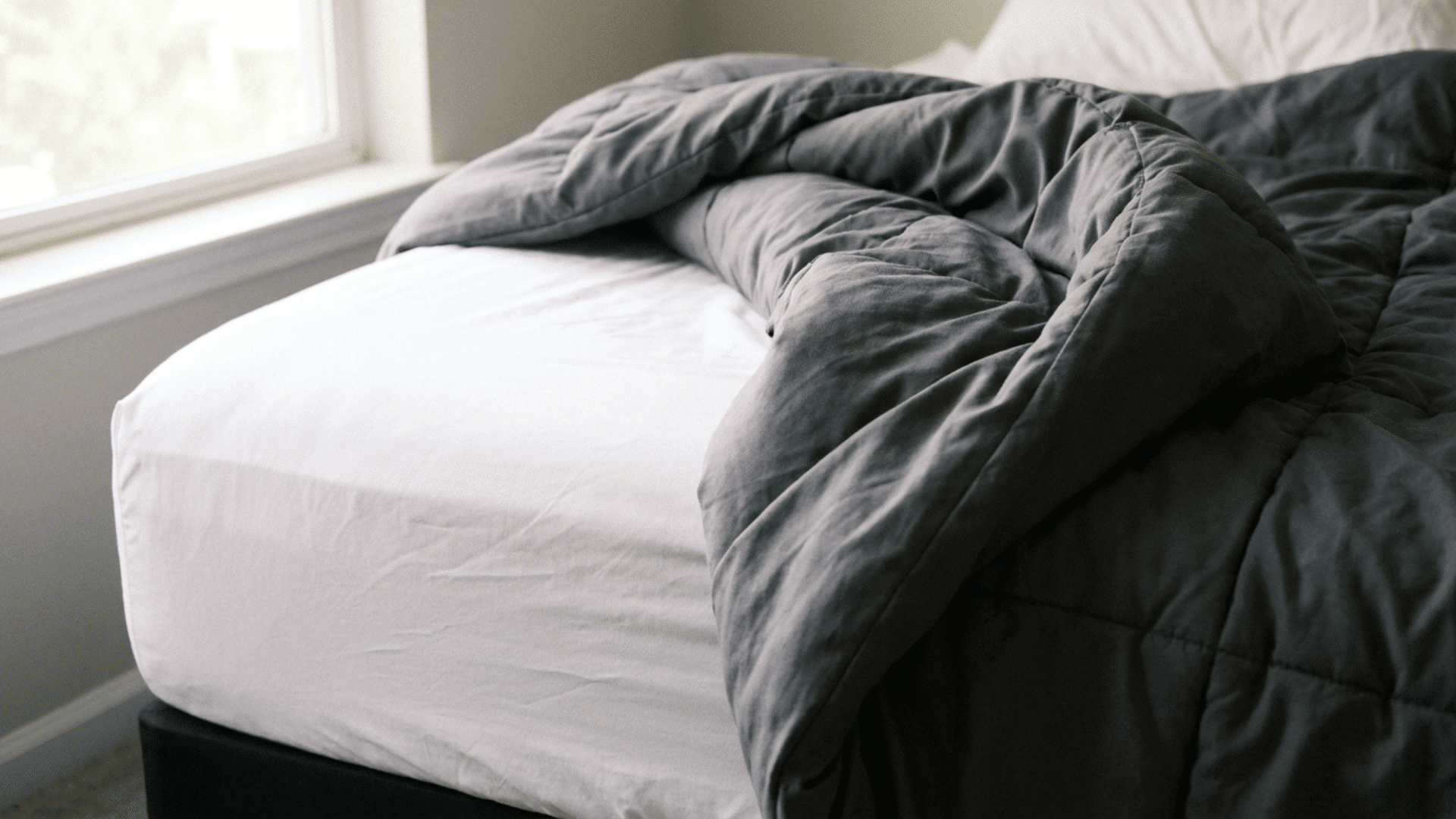 full bed corner showing a snug fitted sheet beneath a loose oversized comforter that shifts