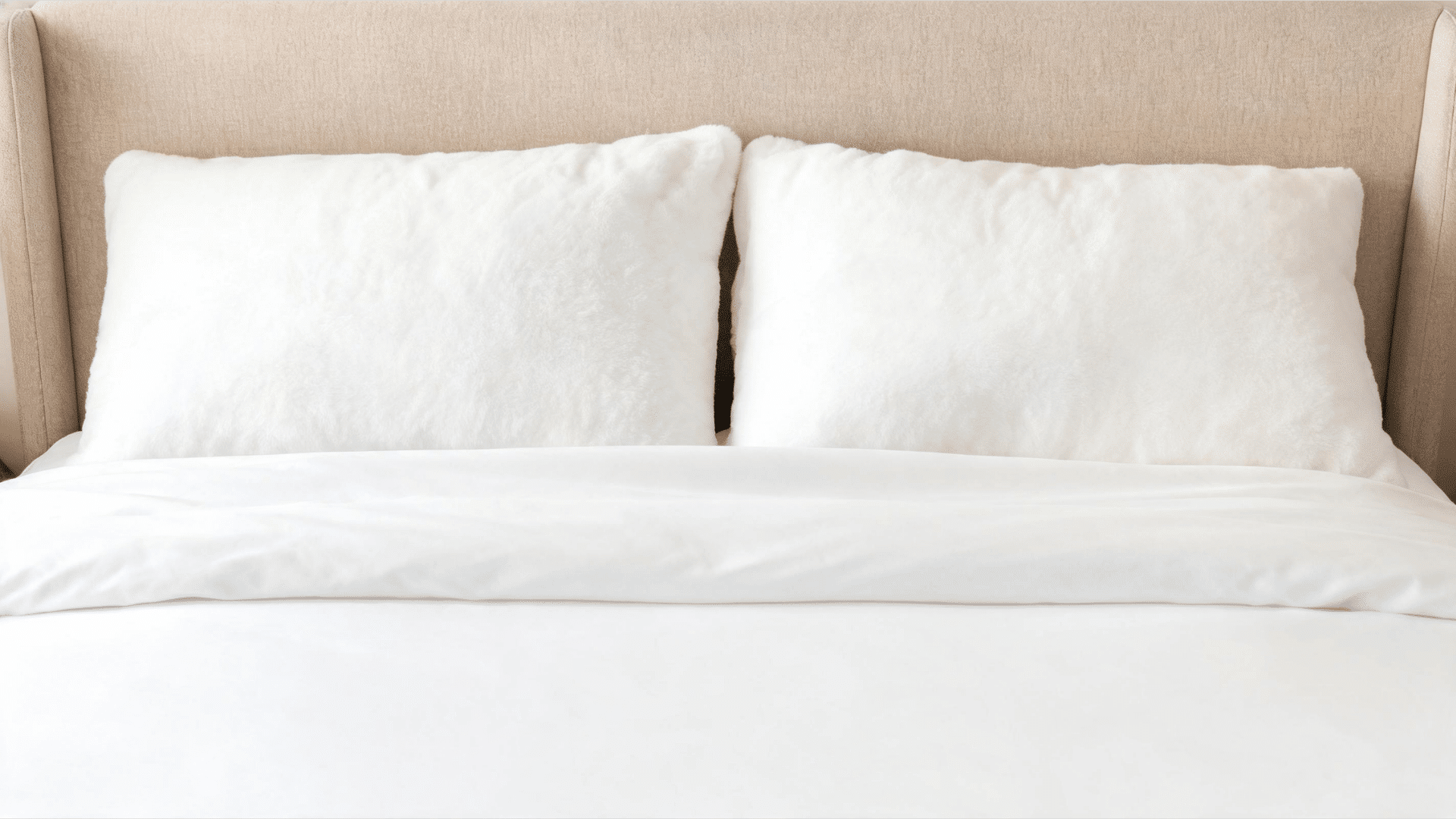 neatly folded bedspread tucked carefully under plush white pillows against a headboard on a perfectly measured full bed