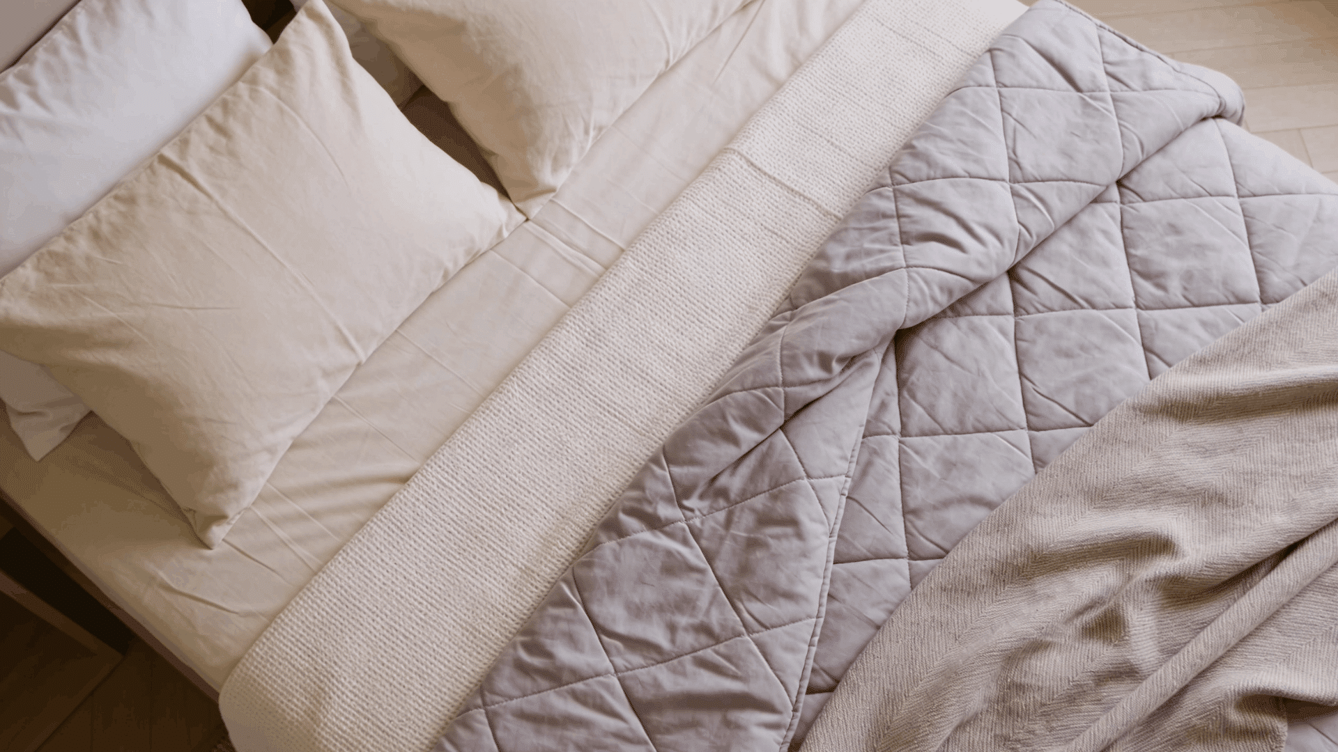 top down view of layered bedding with white pillows cream knit blanket gray quilt and soft beige throw