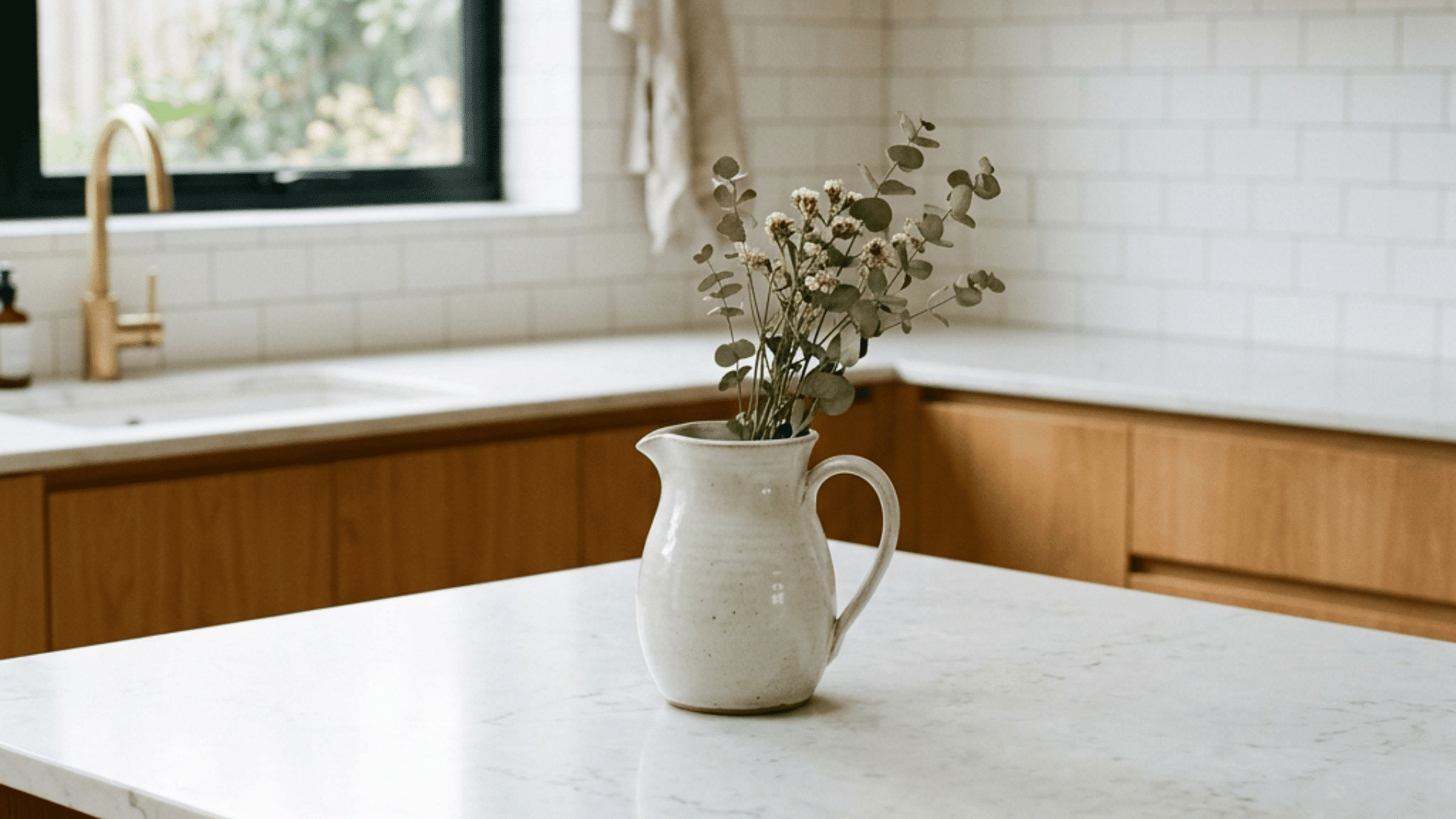 wood kitchen with marble island white pitcher holding greenery and flowers near sink and large window